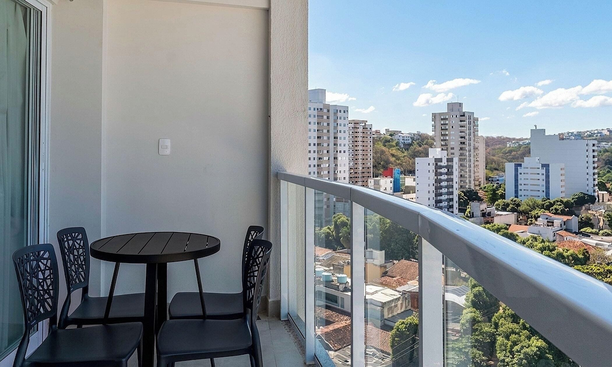 A balcony with a table and chairs, overlooking a cityscape with high-rise buildings.