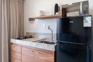 A compact kitchenette with a black refrigerator, a microwave, a gas stove, and a sink. - Well-equipped Studio in Cond. With a Pool Msu1005 (Governador Valadares)