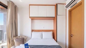 A hotel room with a bed, a wardrobe, an air conditioning unit, and a window with curtains. - Studio in a Cond. With Pool Near the Beach Cao0305 (Salvador)