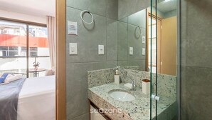 A modern bathroom with a granite countertop, a glass shower enclosure, and a large mirror. - Studio in a Cond. With Pool Near the Beach Cao0305 (Salvador)
