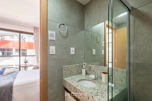 A modern bathroom with a granite countertop, a glass shower enclosure, and a large mirror. - Studio in a Cond. With Pool Near the Beach Cao0305 (Salvador)
