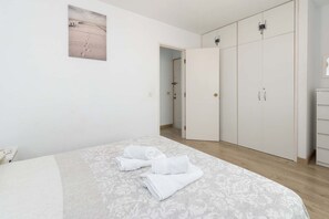 A bedroom with a bed, a wardrobe, and a door leading to another room. - Castle Harbour 42 - One Bed (Los Cristianos)