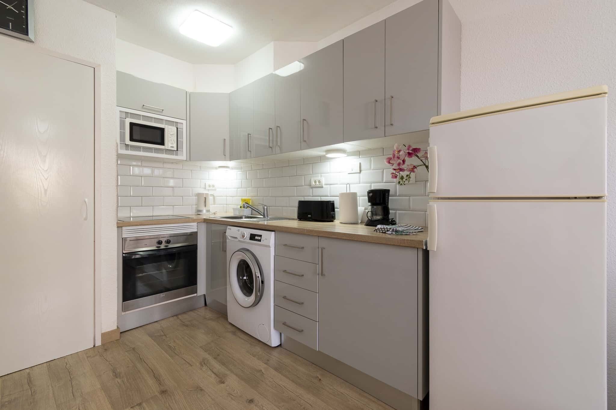 A compact kitchen with a microwave, oven, washing machine, and a coffee maker.