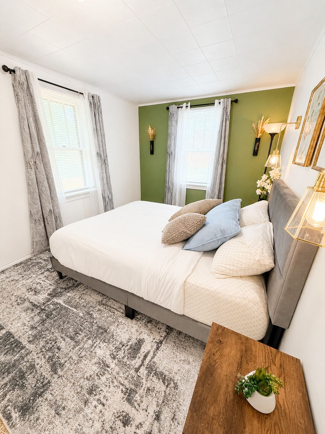 A bedroom with a bed, a nightstand, a lamp, and a wall-mounted shelf with flowers.
