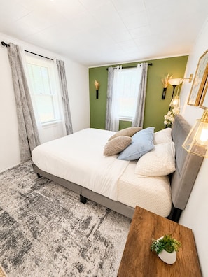 Een slaapkamer met een bed, nachtkastje, lamp en een wandplank met bloemen.