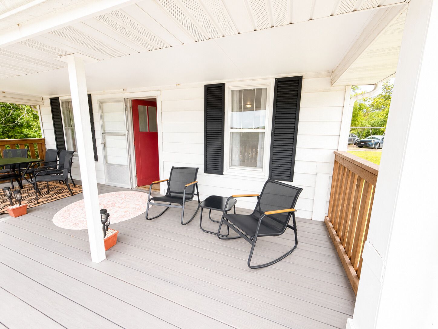 A covered porch with a table and chairs, a red door, and a view of the street.