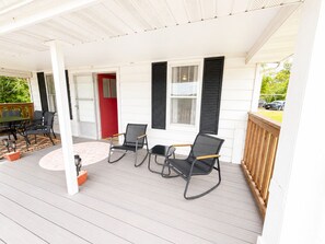 Een overdekte veranda met een tafel en stoelen, een rode deur en uitzicht op de straat.