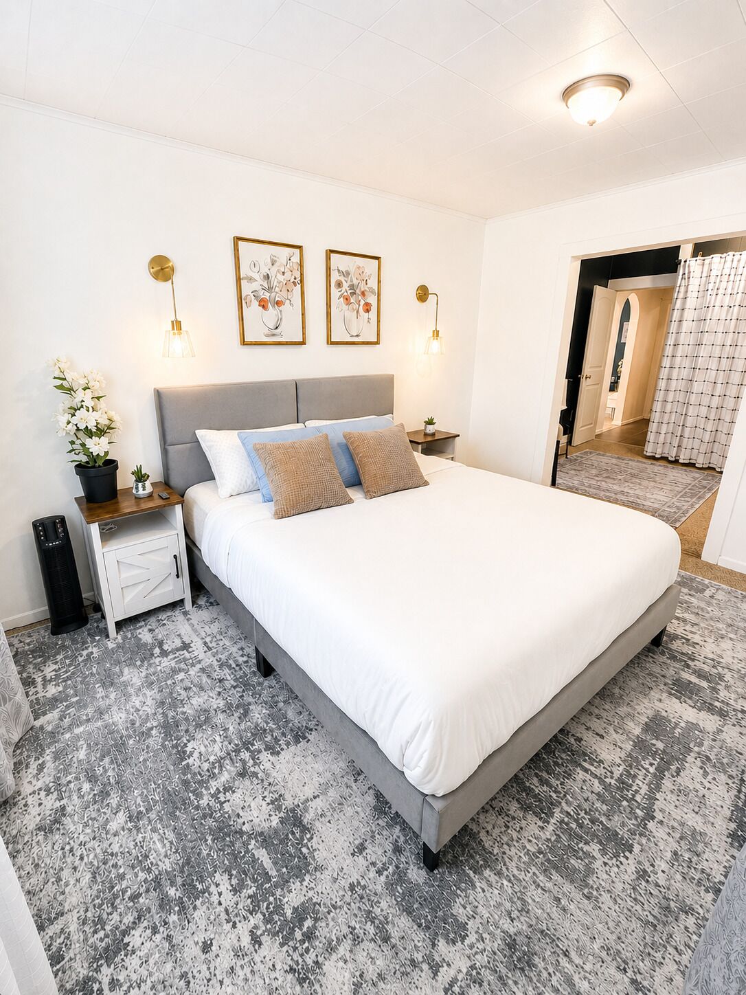 Ein modernes Schlafzimmer mit einem großen Bett, Nachttischen, einer Topfpflanze und gerahmten Kunstwerken an der Wand.