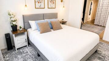 Ein modernes Schlafzimmer mit einem großen Bett, Nachttischen, einer Topfpflanze und gerahmten Kunstwerken an der Wand.