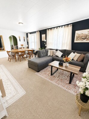 Een woonkamer met een hoekbank, een eettafel met stoelen en een salontafel.
