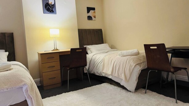 A hotel room with a bed, a desk with a lamp, a chair, and a small rug. - Room-home Away From Home in Salford (Salford)