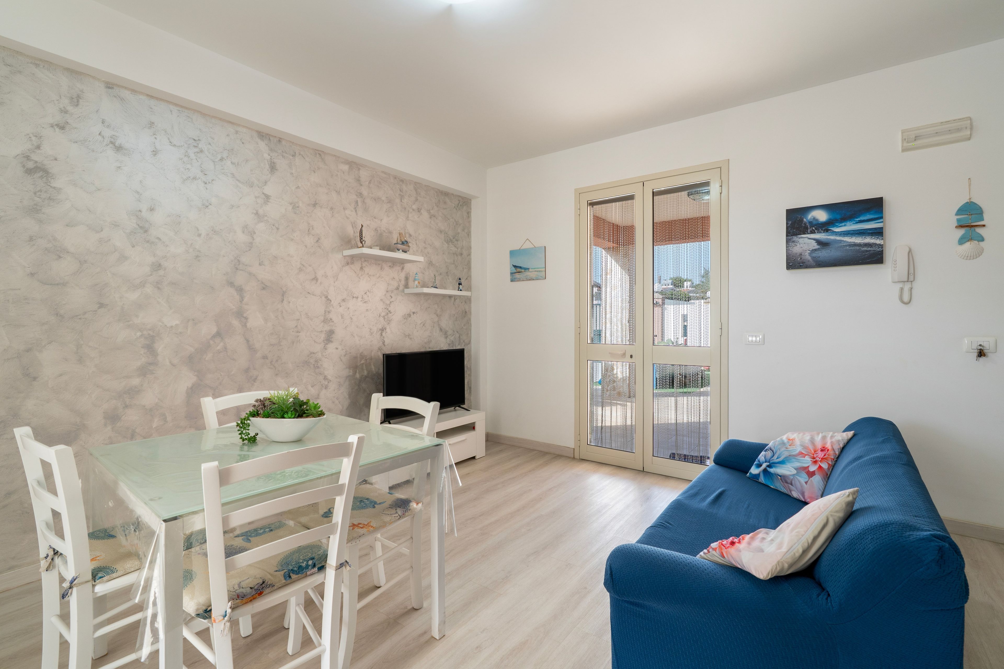 Ein Wohnzimmer mit blauem Sofa, einem Esstisch mit Stühlen, einem Fernseher und einem Balkon mit Aussicht.