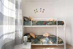 Ein Etagenbett mit tropischem Blattmuster, ein kleiner Nachttisch mit Lampe und Schmetterlingswandsticker.