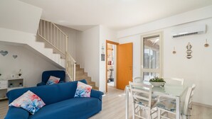 Una sala de estar moderna con un sofá azul, una mesa de comedor con sillas, una escalera y una puerta de madera.