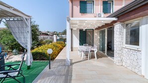 Un espacio de estar al aire libre cubierto, con una mesa, sillas, una pérgola y vistas a una calle residencial.