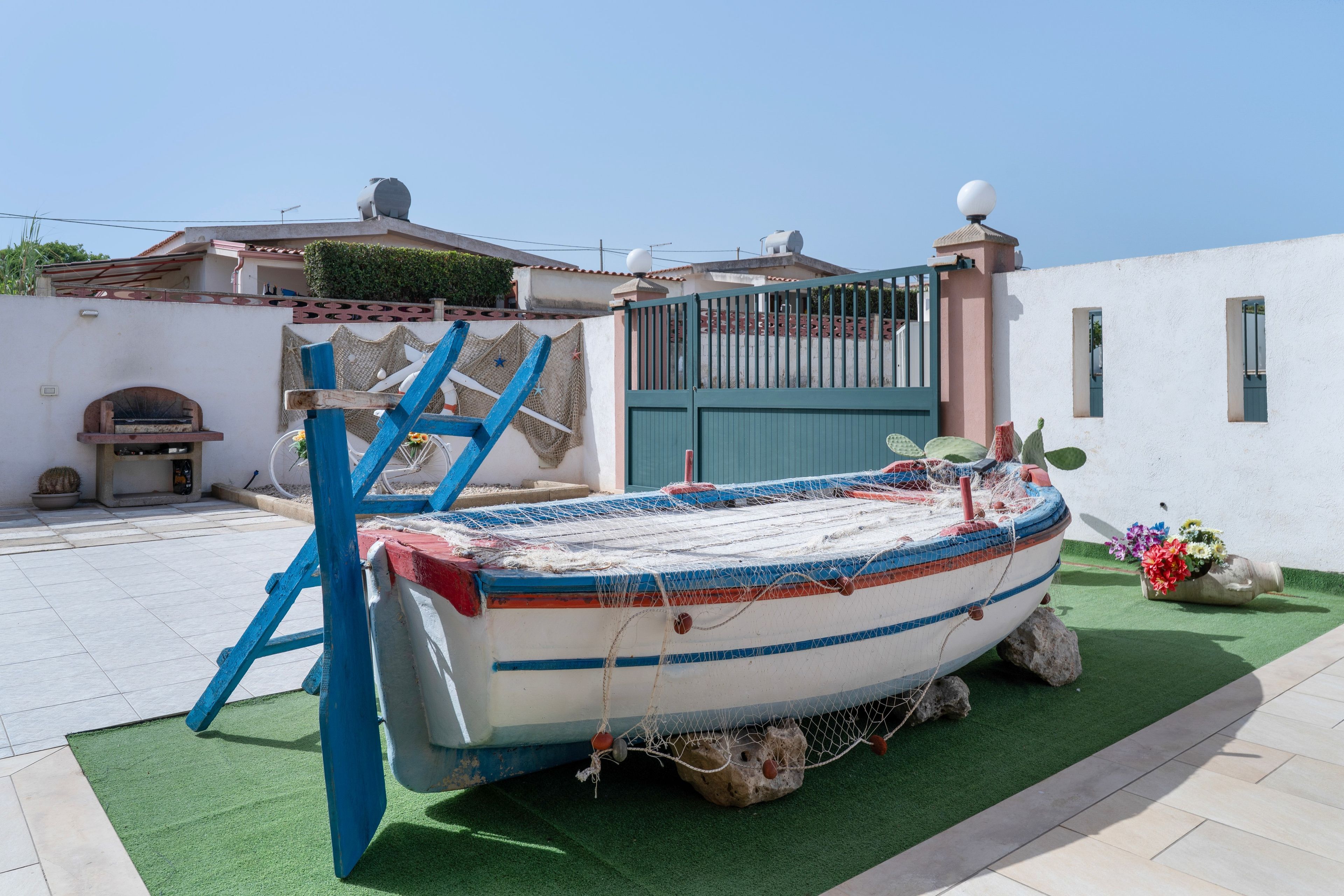 Ein Boot auf Kunstrasen mit einer blauen Leiter, einem Tor und einem Gebäude im Hintergrund.