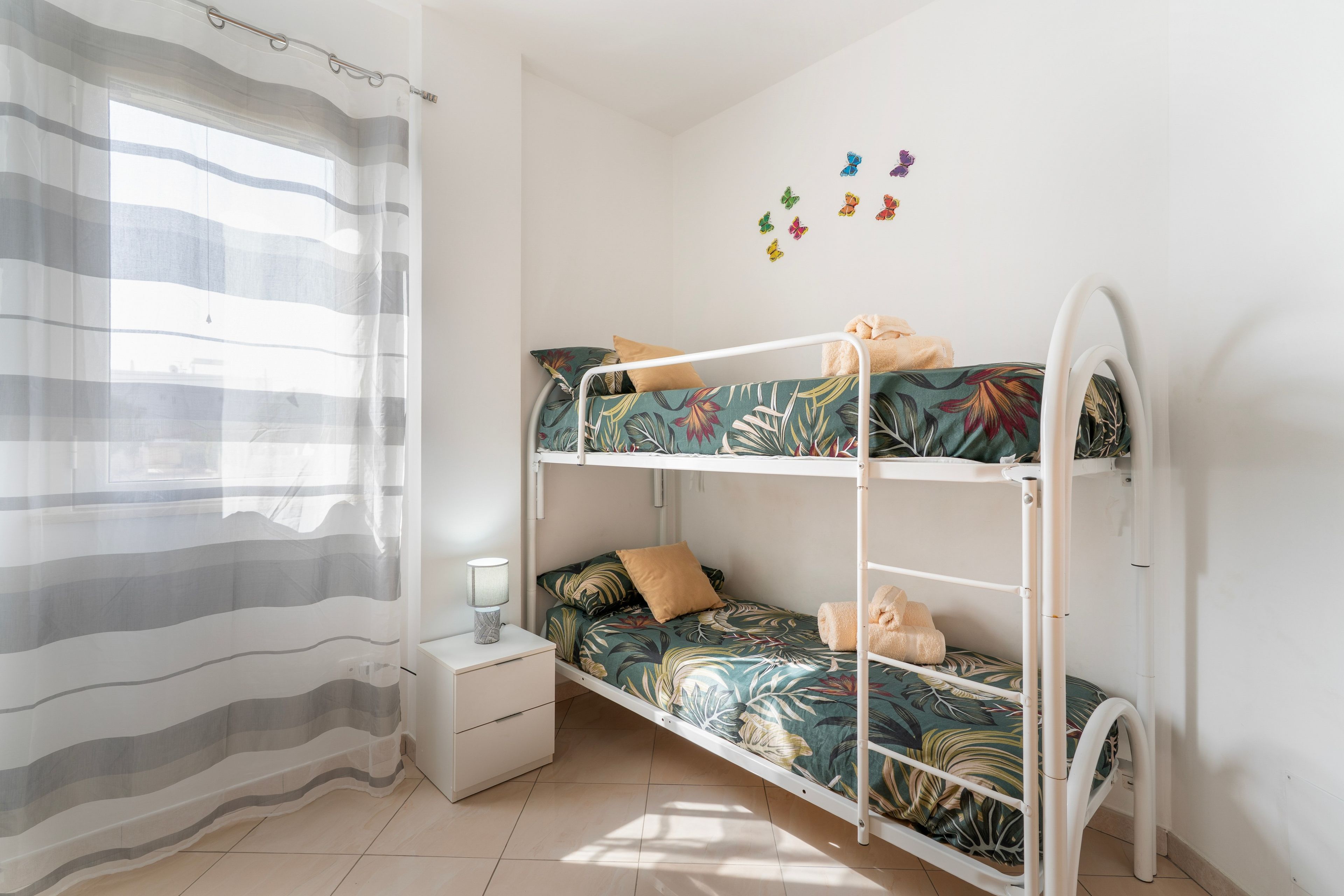 Una cama individual con un edredón estampado con motivos florales, una mesita de noche con una lámpara y una cortina.