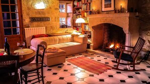 A cozy room with a fireplace, a sofa, a dining table with chairs, and a bookshelf.
