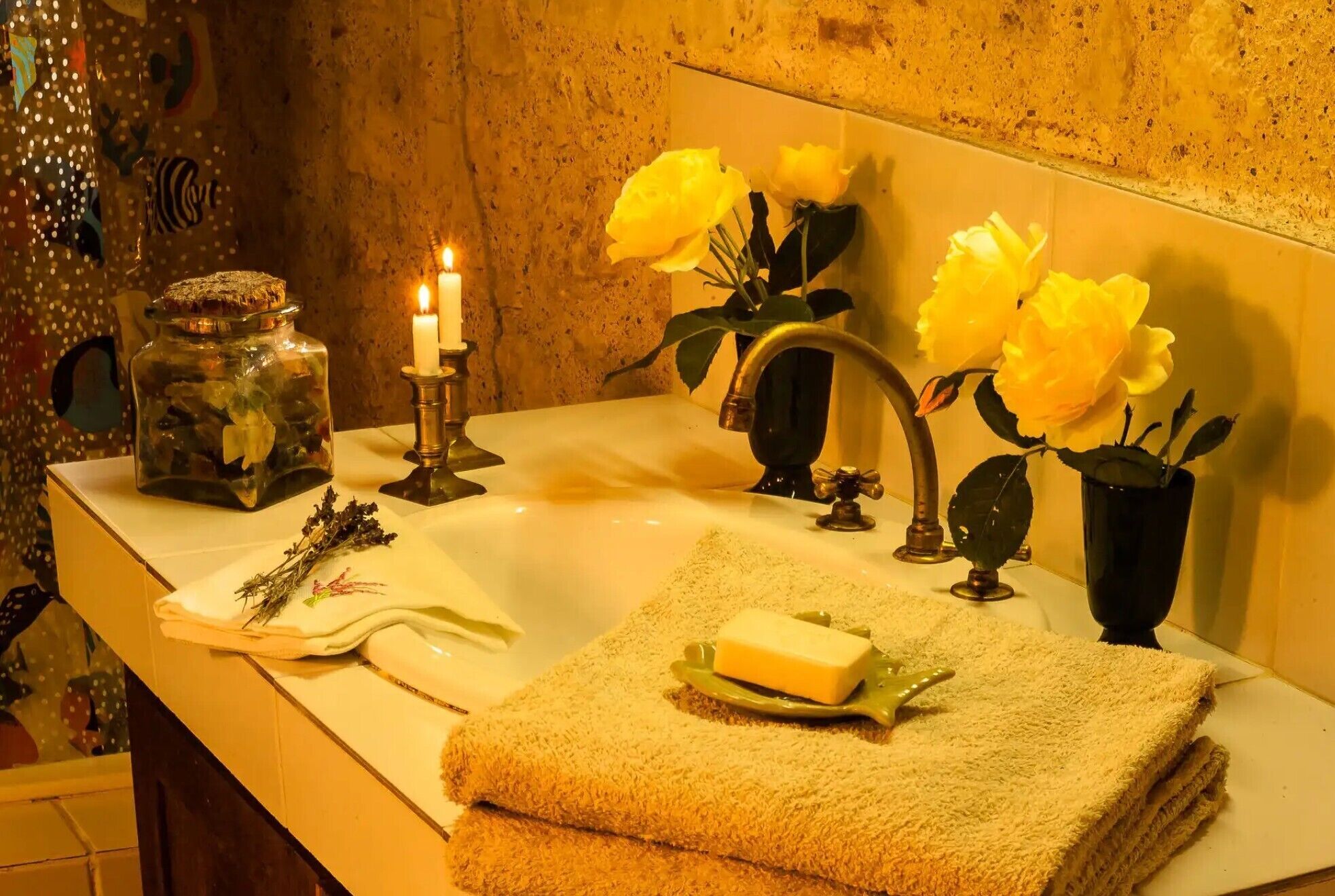 A bathroom with a sink, a mirror, a candle, and yellow flowers.