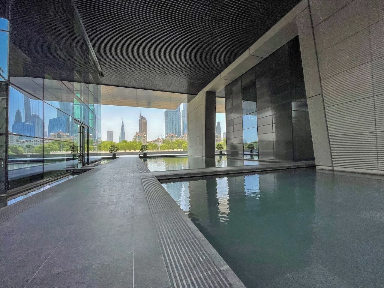Une piscine intérieure moderne avec des parois en verre transparent, un sol carrelé et une vue sur les bâtiments de la ville.