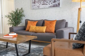 A living room with a grey sofa, two orange cushions, a wooden coffee table, and a framed picture on the wall. - Bright and central Index Tower DIFC by Suiteable (Dubai)