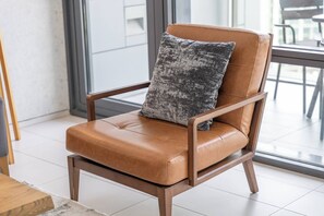 A brown leather chair with a cushion and a textured pillow, positioned in a room with a large window and a tiled floor. - Bright and central Index Tower DIFC by Suiteable (Dubai)