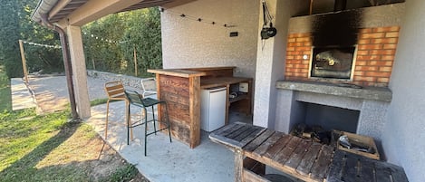 Un patio exterior con una mesa y sillas de madera, un horno de pizza empotrado y un suelo de hormigón.