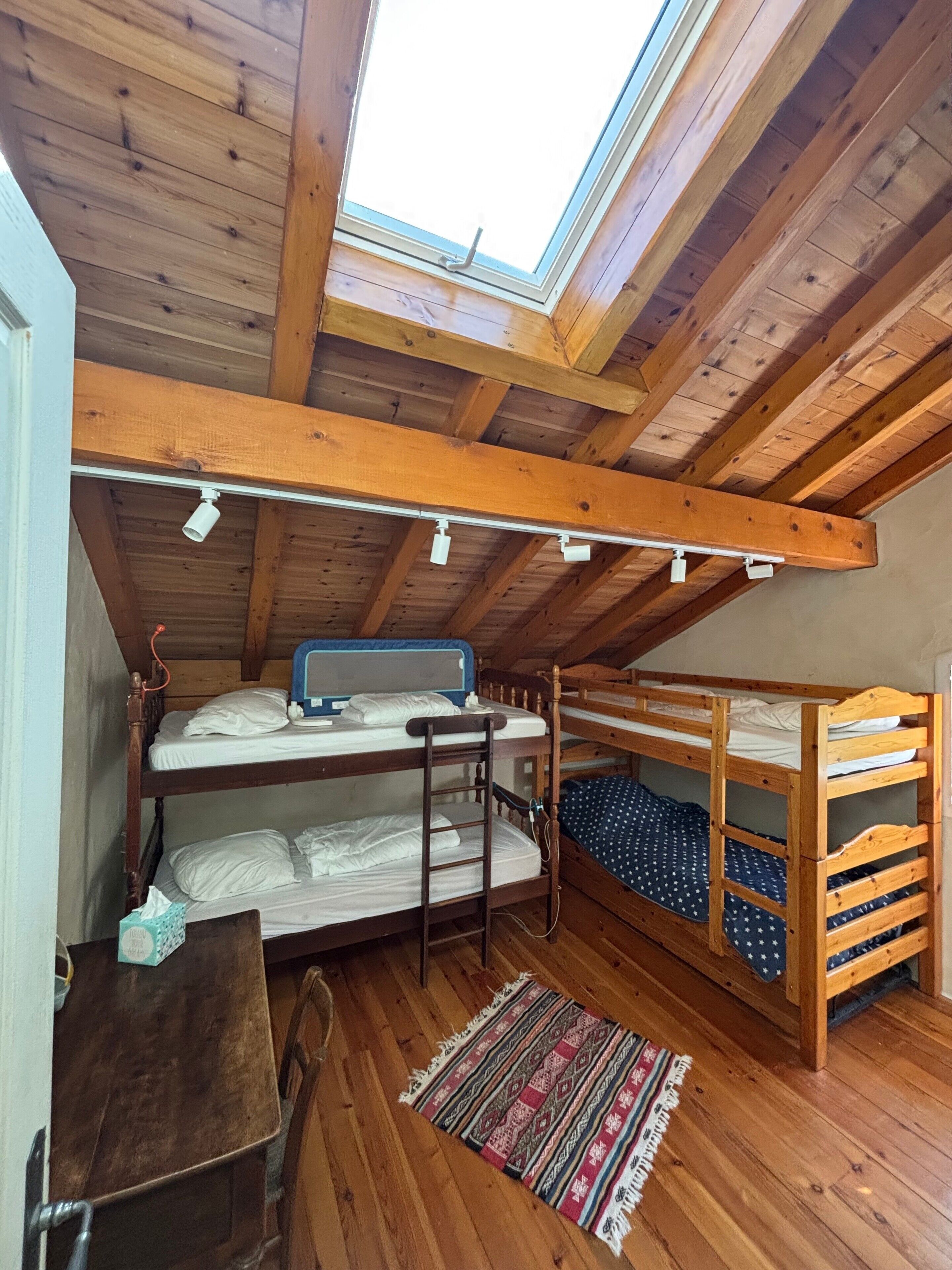 A dormitory-style room with bunk beds, a skylight, and a wooden ceiling.