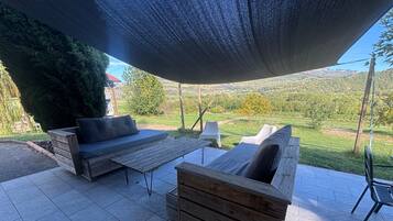 Un área de estar al aire libre con un banco de madera, un sofá, una mesa y un paraguas grande que da sombra.