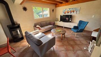 A living room with a sofa, a blue armchair, a coffee table, a fireplace, a television, and a painting on the wall.