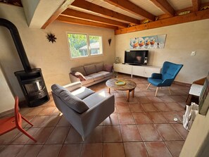 Una sala de estar con un sofá, un sillón azul, una mesa de centro, una chimenea, un televisor y un cuadro en la pared.