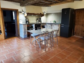 A kitchen with a dining table and chairs, a refrigerator, and a wooden ceiling. - Charming 135 m² Country House, Quiet Setting, Enclosed Garden (Chirassimont)