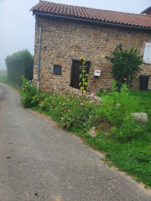 A stone building with a tiled roof, a flower bed with various flowers, and a gravel path. - Charming 135 m² Country House, Quiet Setting, Enclosed Garden (Chirassimont)