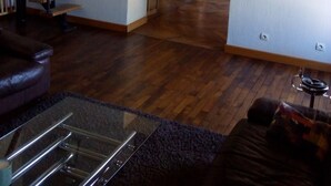 Een ruime woonkamer met een houten trap, een glazen salontafel en een boekenkast.