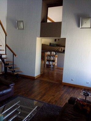 A spacious living area with a wooden staircase, a glass coffee table, and a bookshelf. - Charming 135 m² Country House, Quiet Setting, Enclosed Garden (Chirassimont)