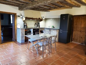 A kitchen with a dining table, chairs, a refrigerator, and a wooden cabinet. - Charming 135 m² Country House, Quiet Setting, Enclosed Garden (Chirassimont)