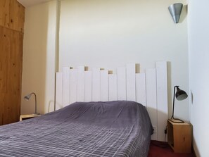 Ein Schlafzimmer mit einem Bett, einem Nachttisch mit Lampe, einem Holzschrank und einer Wandleuchte.
