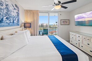 Ein Hotelzimmer mit einem großen Bett, einem Deckenventilator, Blick aufs Meer und einem Bild an der Wand.