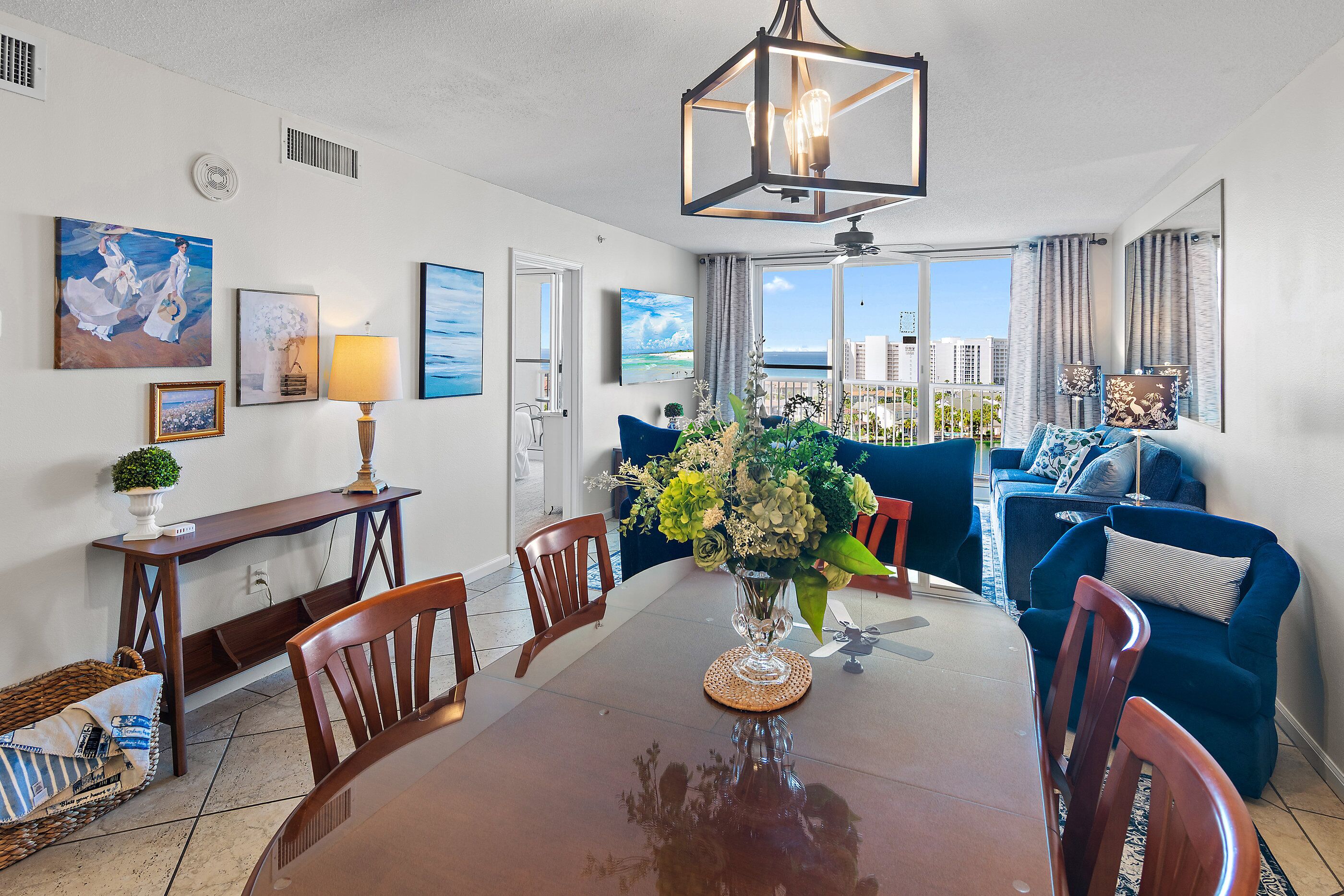 A dining area with a wooden table, chairs, a vase with flowers, and a view of the city through large windows.