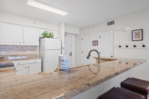 Eine moderne Küche mit weißen Schränken, einer Granit-Arbeitsplatte, einem Edelstahl-Spülbecken und einem eingebauten Backofen.