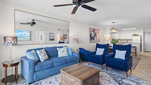 Uma sala de estar com um sofá azul, poltronas combinando, uma mesa de centro de madeira e um ventilador de teto.