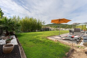 A well-maintained garden with a grassy lawn, potted plants, outdoor furniture, and a large umbrella.