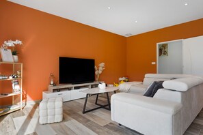 A modern living room with a flat-screen TV, a sofa, a coffee table, and a bookshelf.
