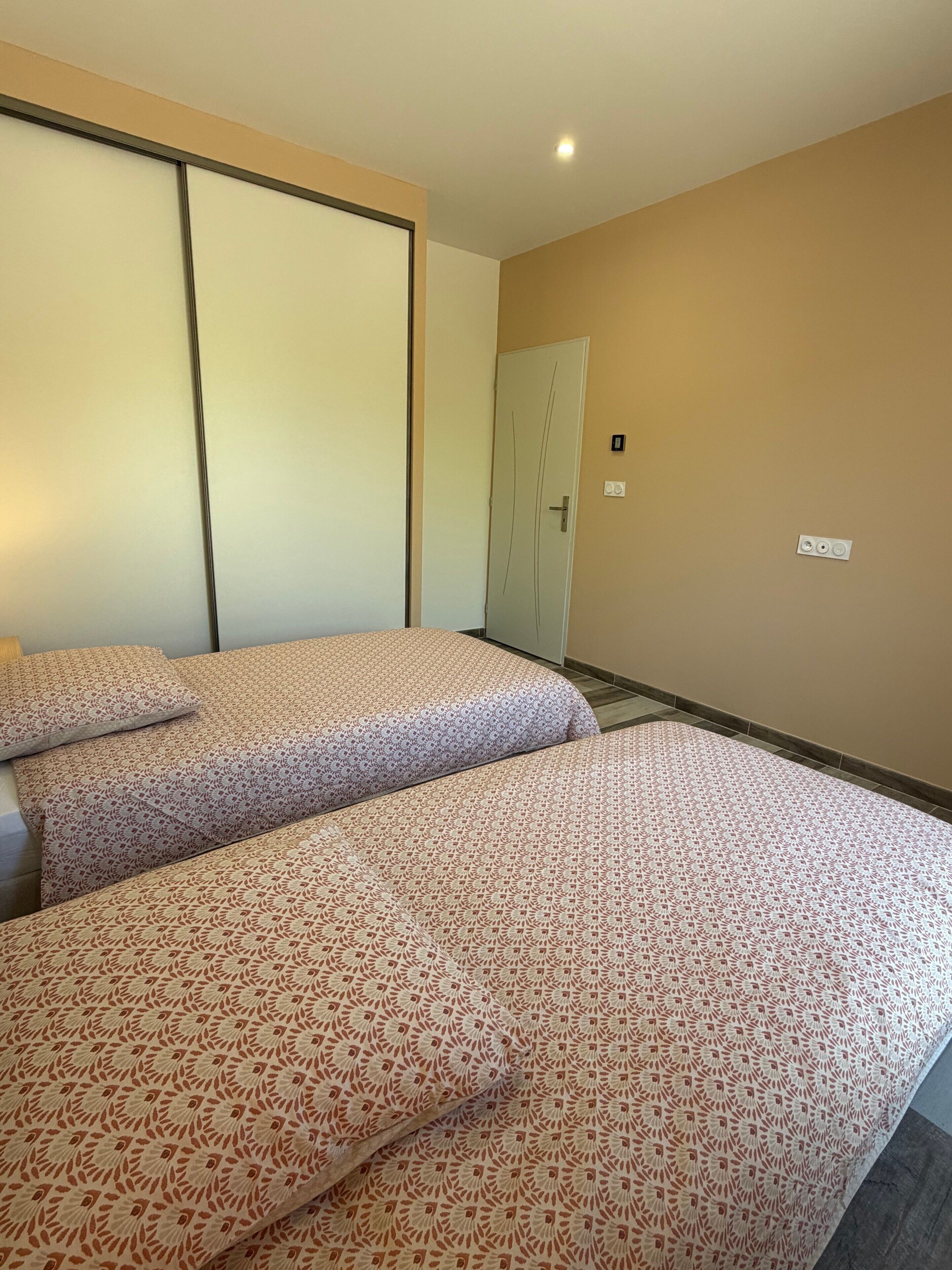Habitación de hotel con dos camas, un armario, una puerta y un interruptor de luz en la pared.