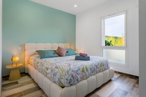 Un dormitorio con una cama, una lámpara de noche, una ventana con vistas y una lámpara de pared.