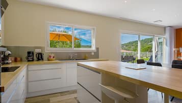 A modern kitchen with a large window, a dining area with a table and chairs, and a view of a green landscape.