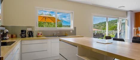 Una cocina moderna con un ventanal grande, un comedor con mesa y sillas, y vistas a un paisaje verde.