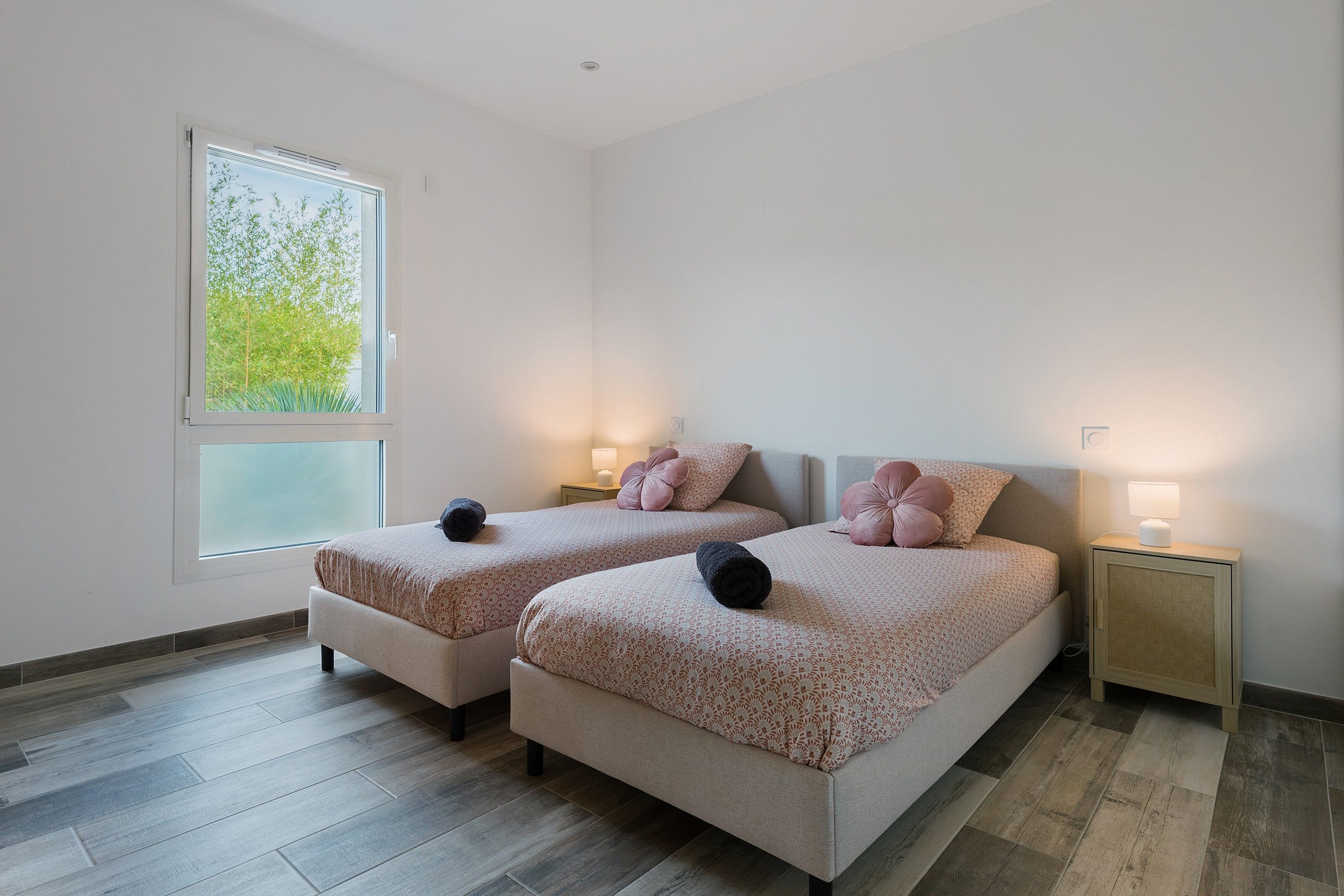 A double room with two beds, a window with a view of greenery, and bedside lamps.