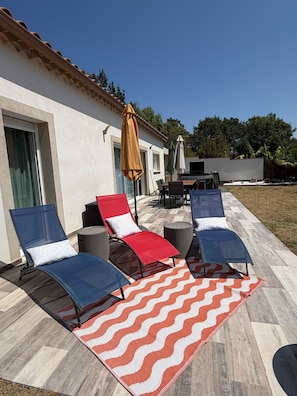 A patio with sun loungers, a patterned rug, and outdoor furniture.