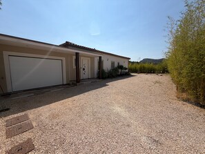A building with a garage door, a gravel driveway, and a landscaped area with trees and shrubs.